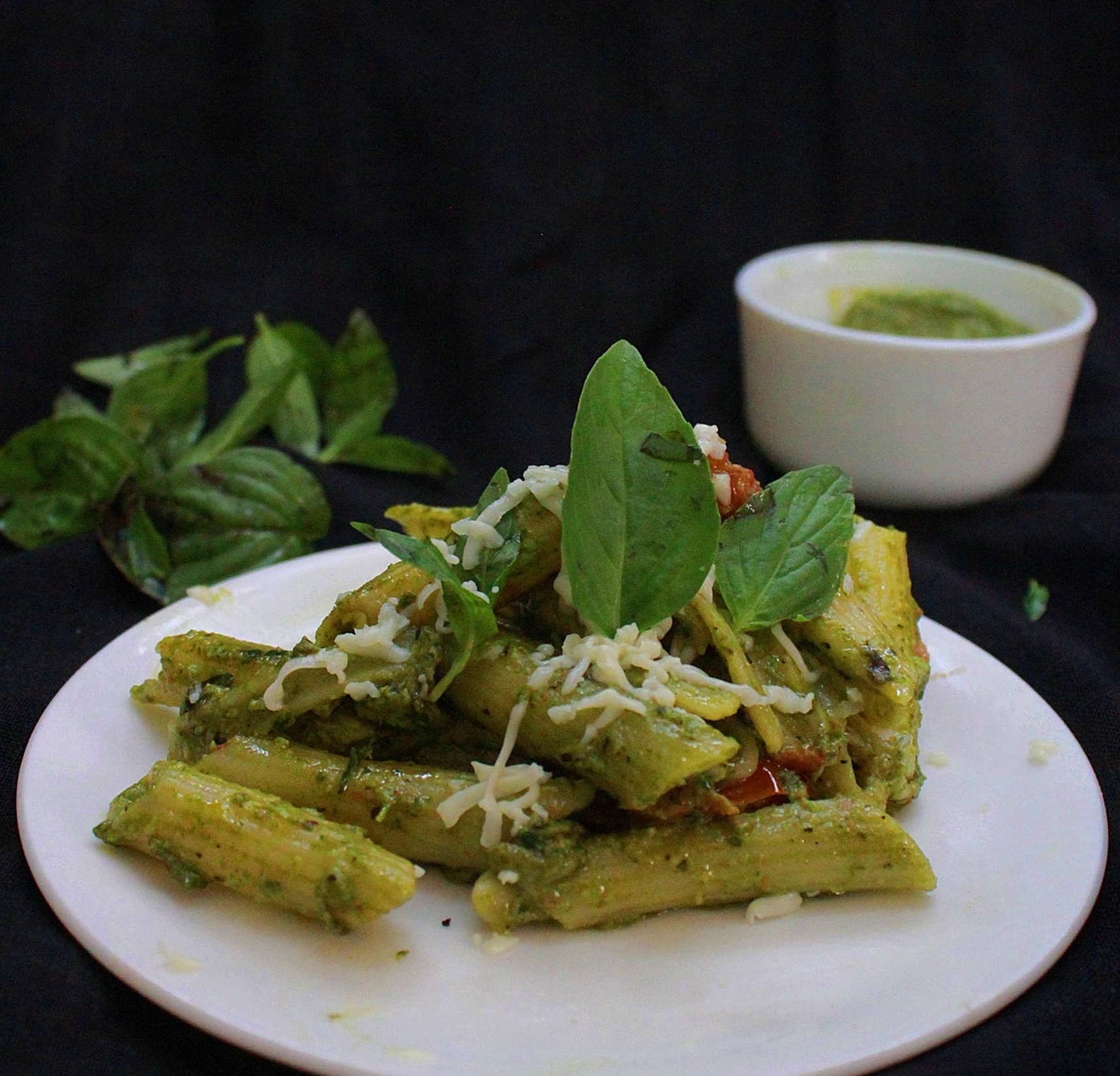 Penne Pasta with Pesto, garnished with cheese and basil leaves.